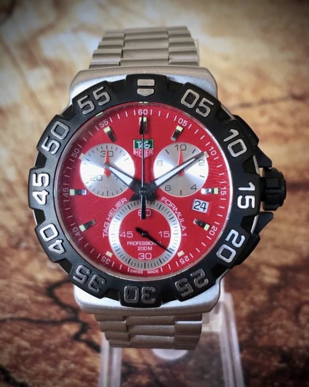 TAG HEUER FORMULA 1, PROFESSIONAL 200M - TEMPPUS: El TAG Heuer Formula 1 con esfera roja es un reloj de diseño deportivo inspirado en el mundo del automovilismo. Pertenece a la icónica colección Formula 1 de la marca, reconocida por sus relojes robustos y funcionales. Este modelo incluye una caja de acero inoxidable de 43 mm de diámetro, y un cristal de zafiro resistente a los arañazos, lo que le otorga durabilidad y una excelente legibilidad. El reloj cuenta con un movimiento de cuarzo, y sus funciones incluyen cronógrafo, horas, minutos, segundos y una ventana para la fecha. La característica esfera roja satinada con efecto “rayos de sol” añade un toque vibrante y dinámico al diseño, mientras que los índices y las manecillas están recubiertos de Super-LumiNova para garantizar la visibilidad en condiciones de poca luz.